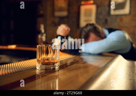 Drunk man sleeping at bar counter with focus on alcoholic drink in glass Stock Photo