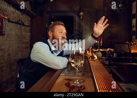Happy smiling drunk man waving hand while sitting at bar counter Stock Photo