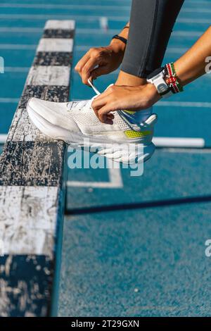 A young runner tying her shoelaces to run over a jumping obstacle on a running track on a sunny day. Stock Photo