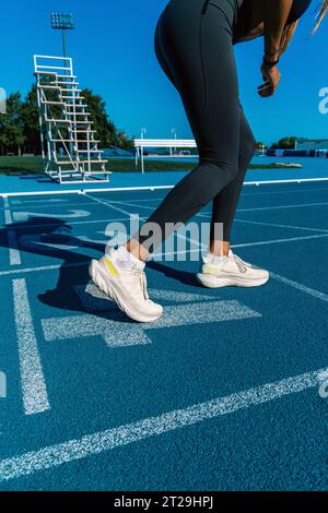Young, tanned woman with long brown hair, prepared in position with her legs bent to do a sprint or race running on a blue athletics track. Stock Photo