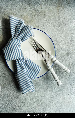 Top view of minimalistic rustic table setting with white plate cutlery and striped napkin on gray surface Stock Photo
