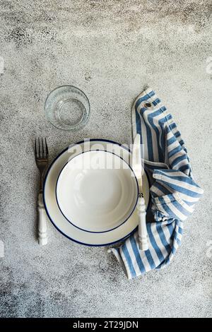Top view of minimalistic rustic table setting with white plates, cutlery, glass and striped napkin on gray surface Stock Photo