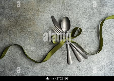 Top view of vintage cutlery set placed on gray surface with green ribbon in light kitchen Stock Photo