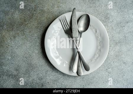 Top view of vintage cutlery set placed on white plate against gray surface in light kitchen Stock Photo