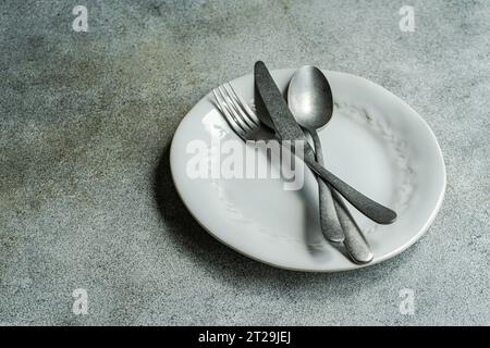 High angle of vintage cutlery set placed on white plate against gray surface in light kitchen Stock Photo