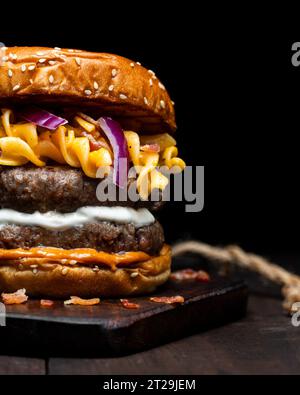 Closeup of crop hamburger with macaroni and cheese placed on wooden tray on table against dark background Stock Photo