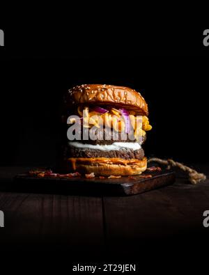 Hamburger with macaroni and cheese placed on wooden tray on table against dark background Stock Photo
