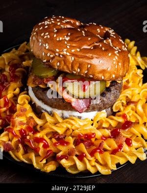 High angle of hamburger placed on plate among macaroni ketchup and cheese against dark background Stock Photo