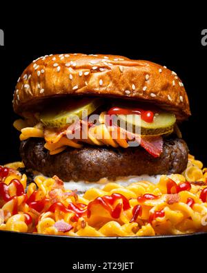 Closeup of hamburger placed on plate among macaroni ketchup and cheese against dark background Stock Photo