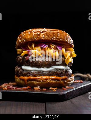 Closeup of hamburger with macaroni and cheese placed on wooden tray on table against dark background Stock Photo