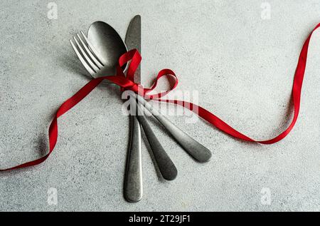 High angle of vintage cutlery set placed on gray surface with red ribbon in light kitchen Stock Photo