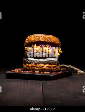 Hamburger with macaroni and cheese placed on wooden tray on table against dark background Stock Photo