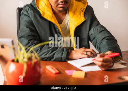 Concentrated ethnic male freelancer in sitting at table and writing in notepad while working on project in office Stock Photo