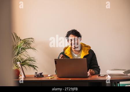 Positive male remote worker using netbook for online project while working on hoffice at table in blurred background Stock Photo