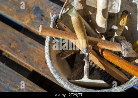 Used construction tools, stored in a bucket, outdoors. View from above, with sunlight illuminating the scene. Stock Photo