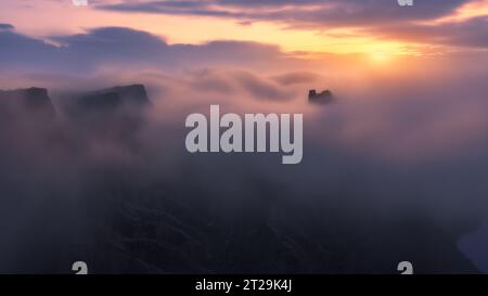 From above drone view of ancient ruined castle mountain peak above clouds on foggy day during sunset in Toledo in Spain Stock Photo