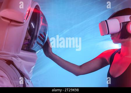 Anonymous male astronaut in spacesuit and woman wearing virtual reality goggles while standing and looking at each other Stock Photo