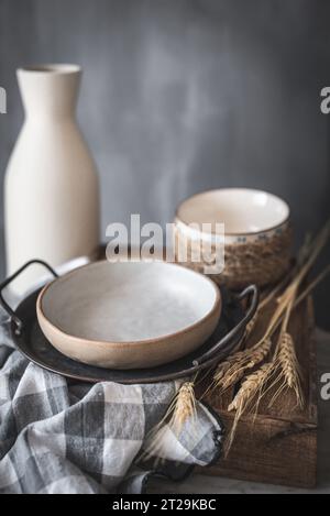 Ceramic bowls and vase near napkin on wooden board placed on marble table against gray background at rustic kitchen Stock Photo