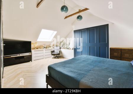 Stylish bedroom with comfortable blue bed and wardrobe with modern television in the corner at attic styled loft Stock Photo