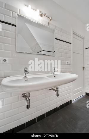 Interior of white bathroom with ceramic sink and mirror mounted on brick tiled wall in modern apartment Stock Photo