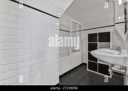 Interior of modern bathroom with ceramic washbasin and black closet in apartment with white tiled walls and floor Stock Photo