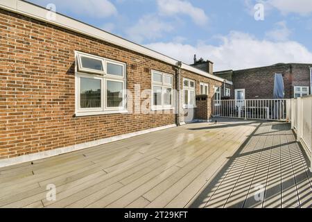 Empty deck in front of building with white windows and brick wall against cloudy sky during sunny day Stock Photo