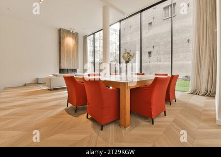 Modern dining room with empty red chairs arranged around wooden table next to large window in contemporary apartment Stock Photo
