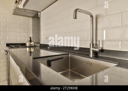 Modern Kitchen with sink and stainless steel faucet in front of white tiled wall and black countertop Stock Photo