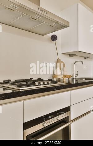 Chrome rangehood over stove on black countertop and white cabinets in modern kitchen at contemporary home Stock Photo