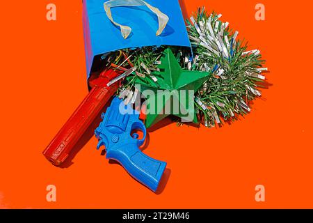 High angle of crop blue carton bag placed on red surface with tinsel, colorful toy guns and green star Stock Photo