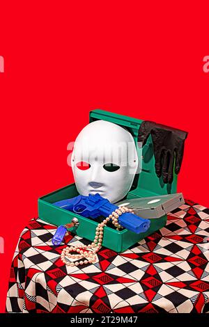 High angle of opened secret box with mask, gloves, toy gun, necklace and video tape placed on table against red wall Stock Photo