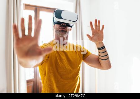 Bearded male in VR goggles standing and stretching arms while training in light apartment Stock Photo