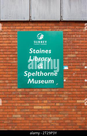 A green sign on a red brick wall for Staines Library and Spelthorne Museum in Staines-upon-Thames, Surrey, UK Stock Photo