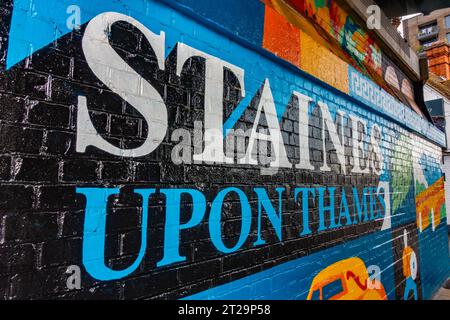 A colourful mural celebrating Staines-upon-Thames on a brick wall under a railway bridge on The High Street in Staines. Stock Photo