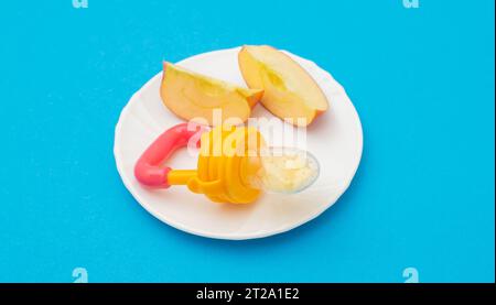 A cut apple on a plate and a baby nibbler on a blue background. The concept of feeding children fruits and vitamins, teething Stock Photo