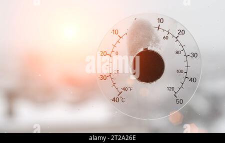 The rays of the setting sun in the sky against the background of a street thermometer with a snow cap on the window. Snowy weather and warming concept Stock Photo