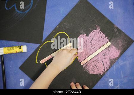 Kids chalk drawing. Kids colouring on black paper using chalk technique. Stock Photo