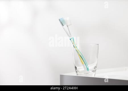 Green and yellow toothbrush in glass on a white table. Stock Photo