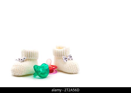 Knitted baby booties with bows in black polka dots and turquoise and pink pacifiers on isolated white background. Background. For text. For design. Stock Photo