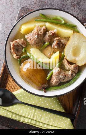 Homemade stew made from lamb meat, fresh pears, potatoes, green beans close-up in a bowl on a wooden board. Vertical top view from above Stock Photo