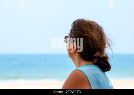 Life is a beach: A middle-aged woman of Indian descent sits in quiet contemplation looking out to the beach and turquoise ocean in Mui Ne, Vietnam. Stock Photo