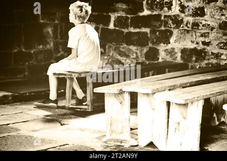 Little boy praying in old chapel. Retro aged photo. Sepia. Stock Photo