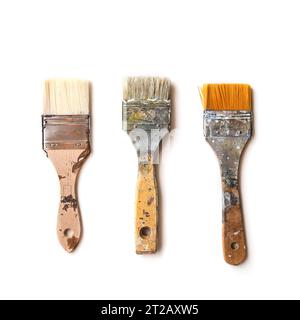 Three used flat brushes in a row for paint, lacquer, varnish or stain isolated with shadows on a white background, copy space, top view from above, se Stock Photo