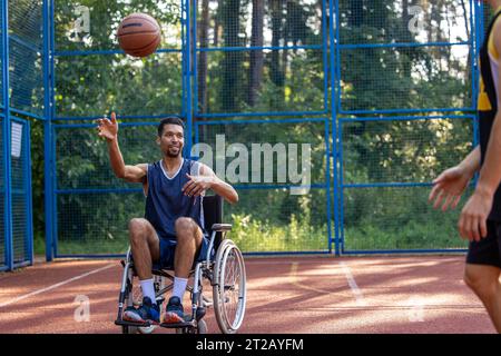 Basketball players playing the match while black guy using wheelchairs on sports court. Stock Photo