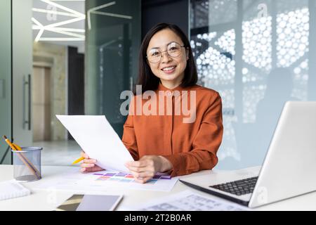 Successful Asian woman doing paperwork inside the office, businesswoman holding documents, reports and papers in her hands, smiling and looking at the Stock Photo