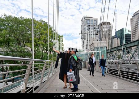 A young couple both dressed in gown and mortar taking a selfie on the South Bank walkway, having just attended a graduation ceremony, Waterloo London. Stock Photo