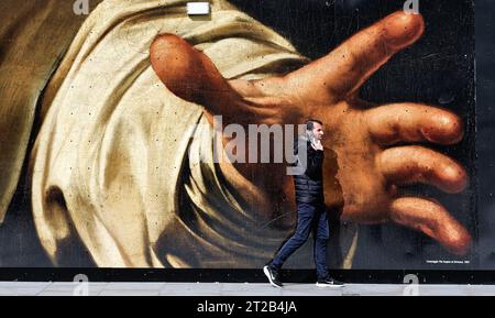 Pedestrian walking past a large reproduction of a painting by Caravaggio depicting a large grabbing hand, on a hoarding in central London England UK Stock Photo