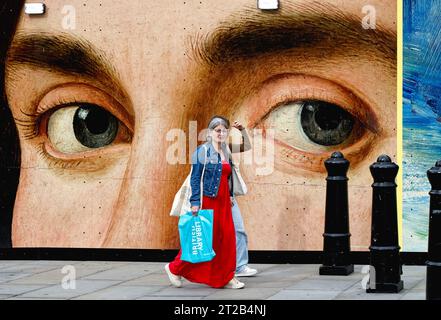 Two women walking by a close up of a pair of eyes from a painting by Antonello de Messina on a poster central London England UK Stock Photo