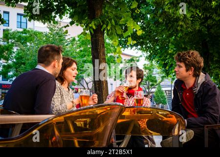 Four young adults talk and drink beer together at an outdoor restaurant in Lyon, France. Stock Photo
