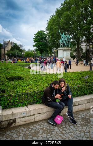 A young couple look at a mobile phone while many people mill about a landmark statue in Paris, France. Stock Photo